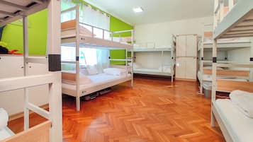 A dormitory room with bunk beds, wooden flooring, and a green accent wall.