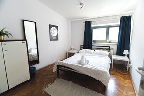 A hotel room with a bed, a nightstand, a desk, a wardrobe, a window with curtains, and a wall-mounted mirror. - Whole Wide World Hostel & Bar (Zagreb)
