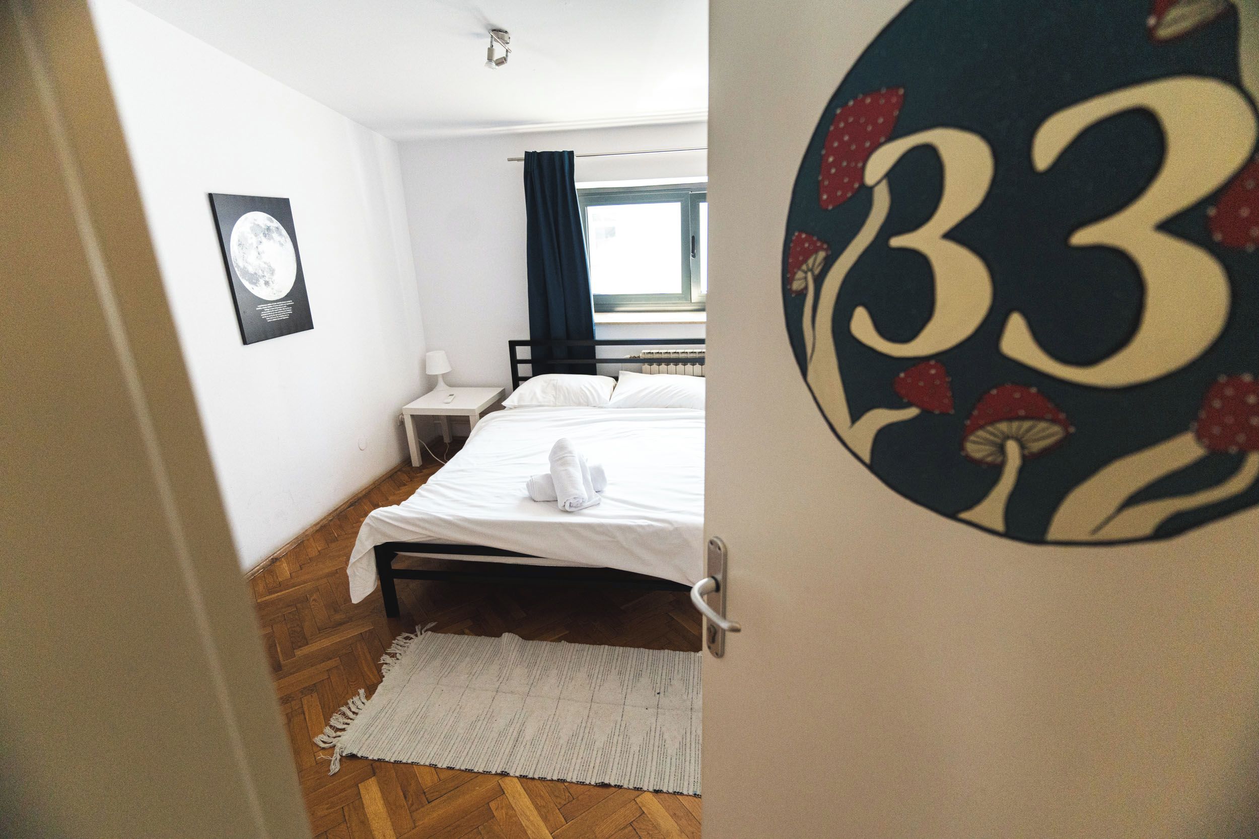 A bedroom with a bed, a nightstand, a wall clock, and a window with curtains.