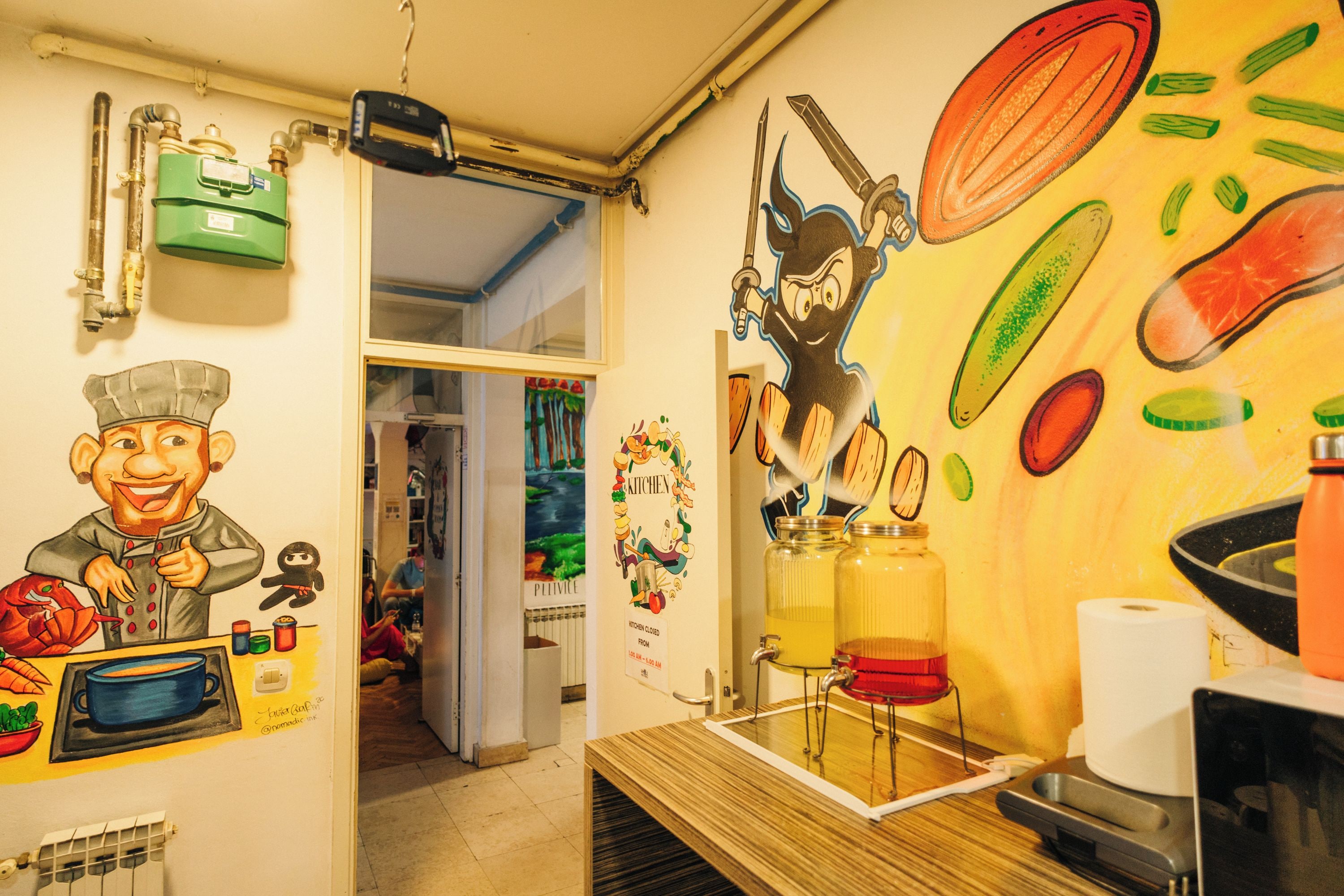 A kitchen with a mural, a green water heater, and a red sink.