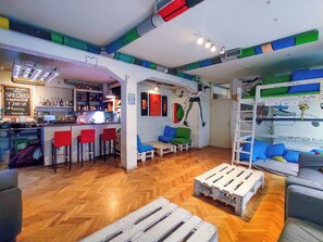 A bar area with stools, a counter, and a seating area with cushions. - Whole Wide World Hostel & Bar (Zagreb)