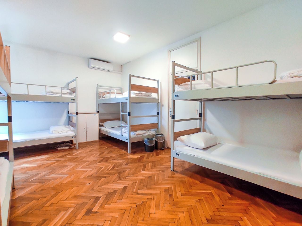Un dormitorio con literas, suelo de madera y una pared blanca con unidad de aire acondicionado.