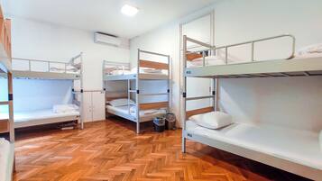 Un dormitorio con literas, suelo de madera y una pared blanca con unidad de aire acondicionado.