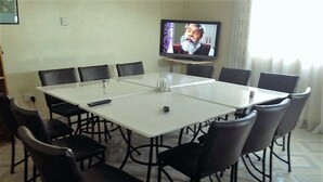 A conference room with a large table, black chairs, a television on the wall, and a window with curtains. - Nairobi Transit Lounge (Syokimau)