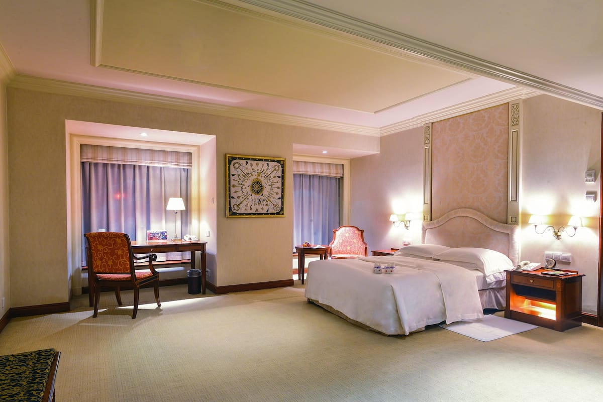 Una habitación de hotel con cama, escritorio, silla, mesita de noche y lámpara.