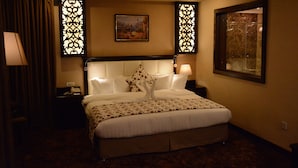 A hotel room with a large bed, a nightstand, a lamp, and decorative panels. - Rojina Hotel (Amman)