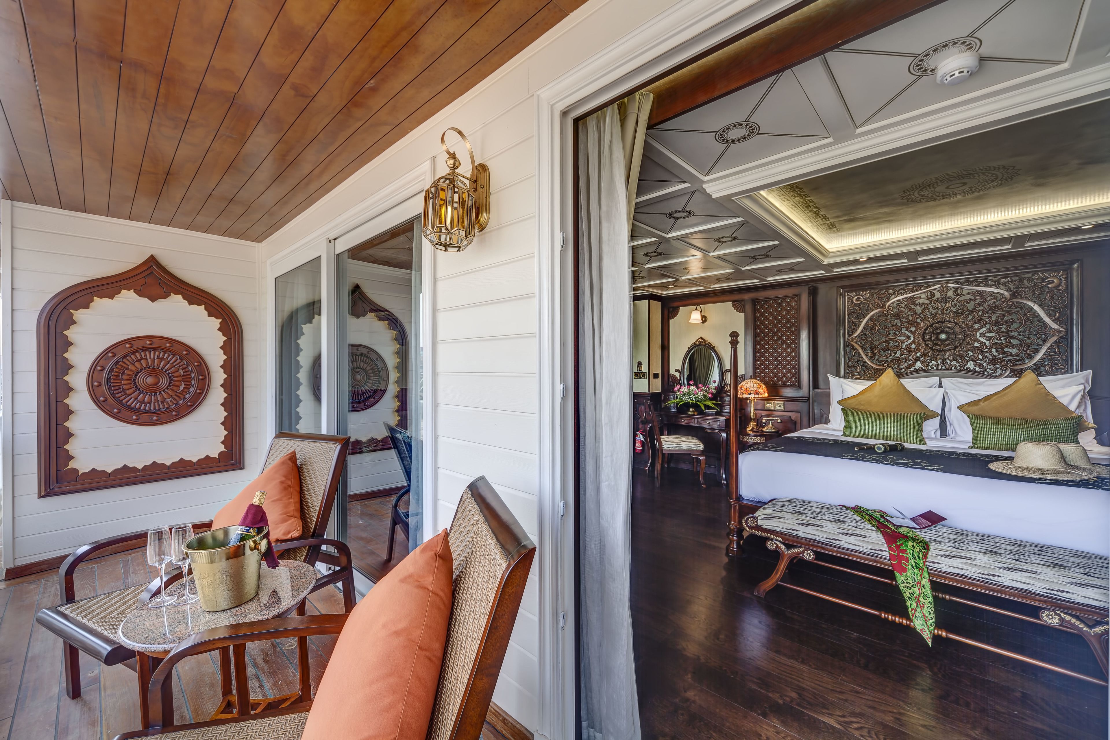 A room with a wooden ceiling, a bed with green and white bedding, a bench with a green cloth, and a wall with a decorative mirror and a circular design.