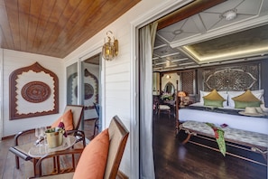 Una habitación con techo de madera, una cama con ropa de cama verde y blanca, un banco con tela verde y una pared con un espejo decorativo y un diseño circular.