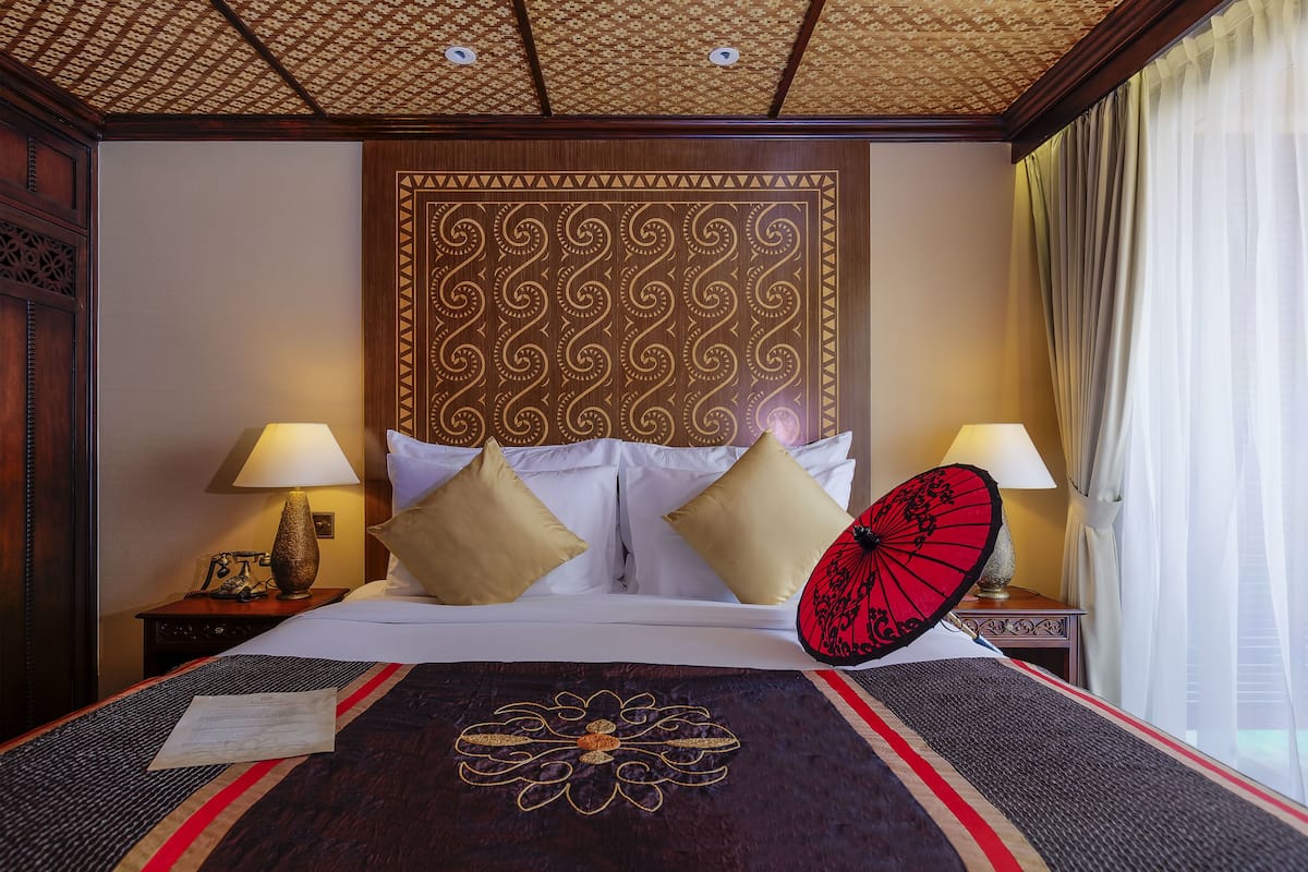 Ein Hotelzimmer mit einem großen Bett, zwei Nachttischlampen, einem dekorativen Kopfteil, einem roten Regenschirm und einer Tagesdecke mit Blumenmuster.