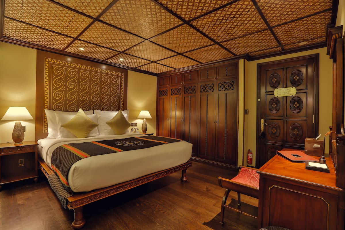 Ein Hotelzimmer mit einem großen Bett, einem Holzschrank, einem Schreibtisch und einer gemusterten Decke.