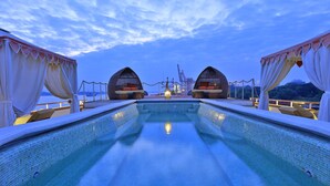 Zona de piscina con vista despejada al agua, dos grandes estructuras en arco y una vista distante del mar y grúas.