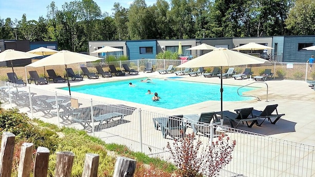 A swimming pool with lounge chairs and umbrellas, surrounded by a fence and wooden posts. - Terres de France - Domaine du Moulin Neuf (Malansac)