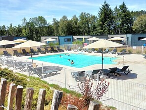 A swimming pool with lounge chairs and umbrellas, surrounded by a fence and wooden posts.