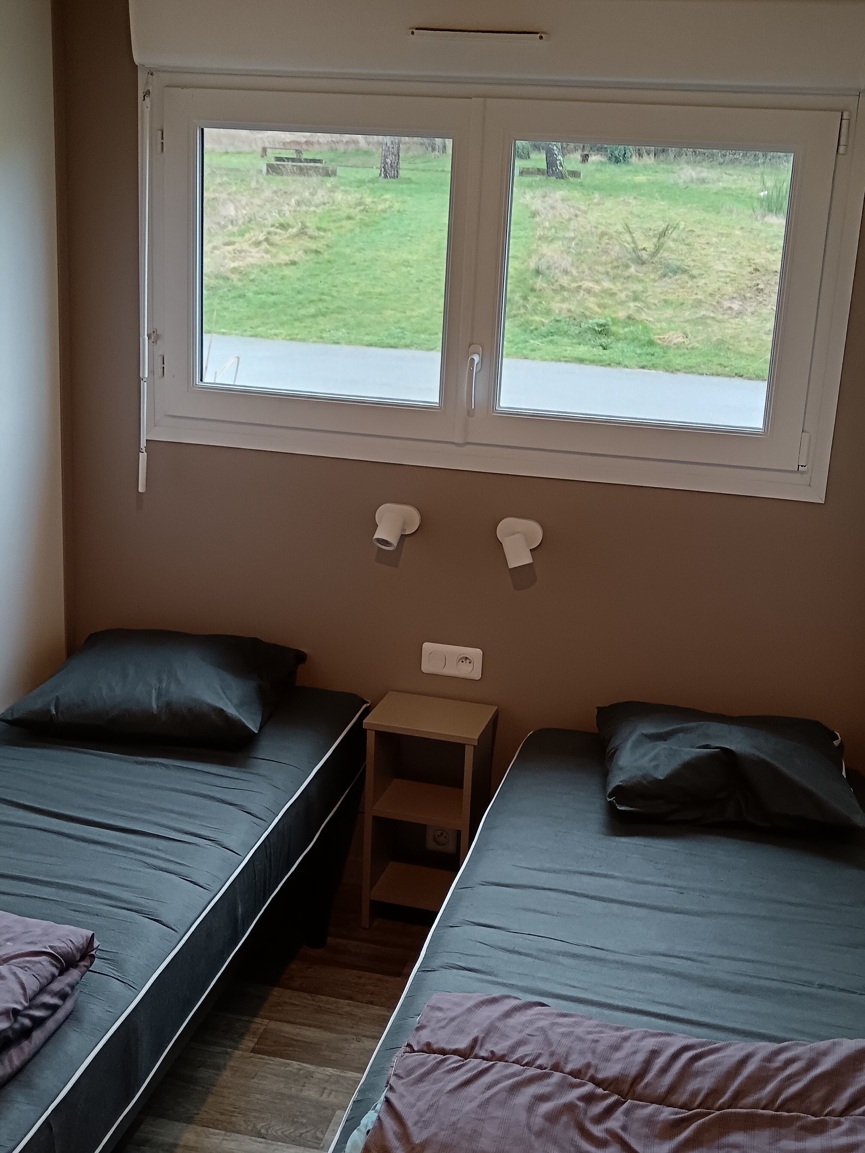 Een kamer met twee eenpersoonsbedden, een klein houten nachtkastje en een raam met uitzicht op een grasveld.