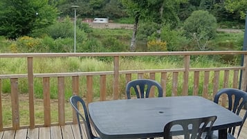 A wooden deck with a table and chairs, overlooking a lush green landscape and a body of water.