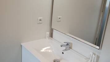 Un baño moderno con un lavabo blanco, un espejo y un mueble con cajón.