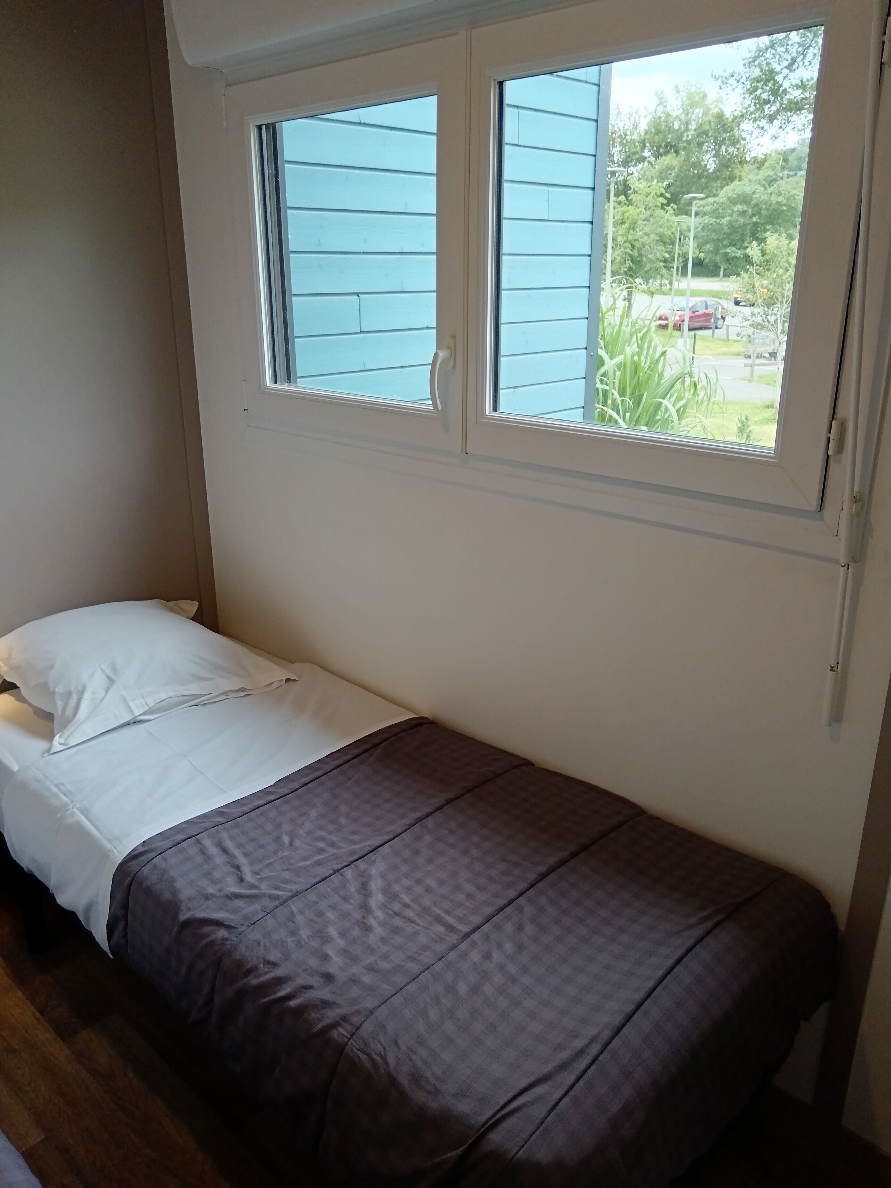 Una habitación pequeña con cama individual y ventana con vistas a un jardín.