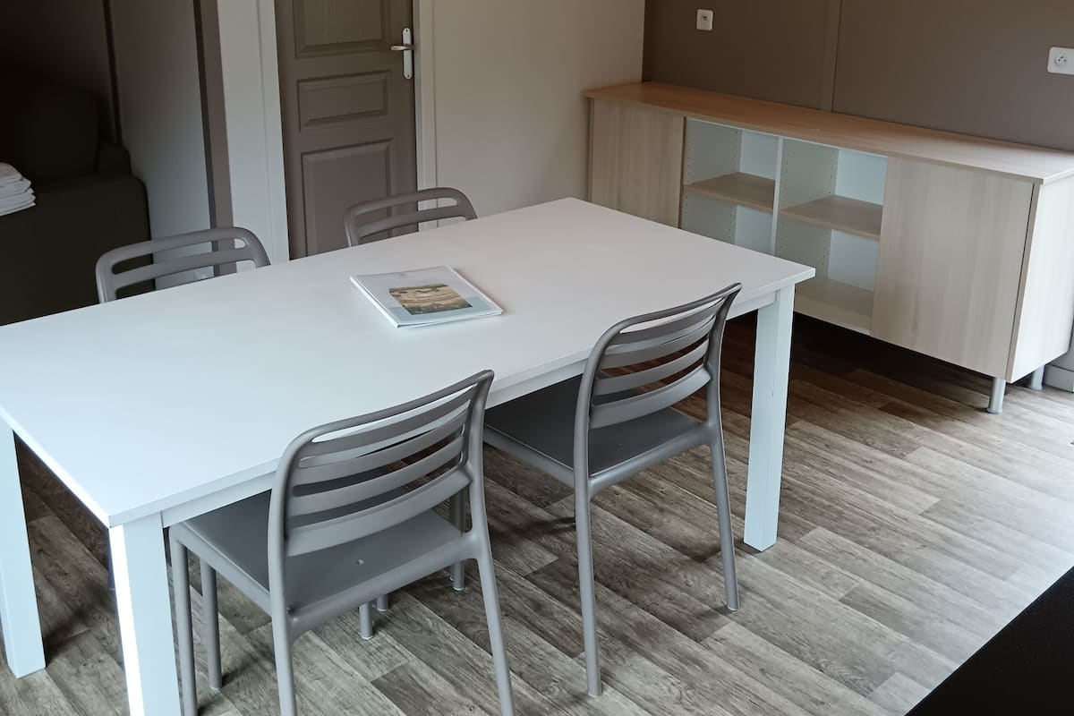 Ein Essbereich mit einem weißen Tisch, vier Stühlen, einem Holzschrank und einer Tür.