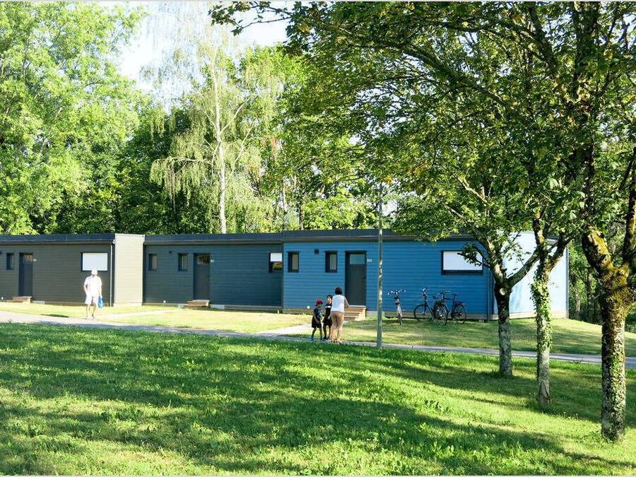 A row of blue and grey buildings with a grassy area in front, bicycles parked, and trees in the background.