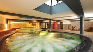 A hot tub area with multiple seating options and a stone wall backdrop. - Hotel Palota Lillafüred (Miskolc)