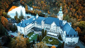 An aerial view of a large, historic building with multiple wings, surrounded by a forested area and a body of water. - Hotel Palota Lillafüred (Miskolc)