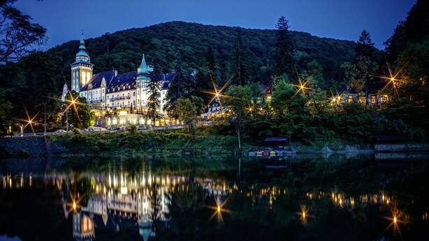 A historic building with a tower, surrounded by trees and a lake. - Hotel Palota Lillafüred (Miskolc)
