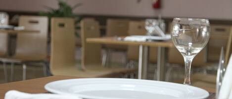 Una mesa de comedor con un plato blanco, una servilleta doblada y una copa de vino transparente.