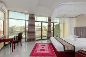 Habitación de hotel con una cama grande, un escritorio y vistas de la ciudad a través de amplios ventanales.