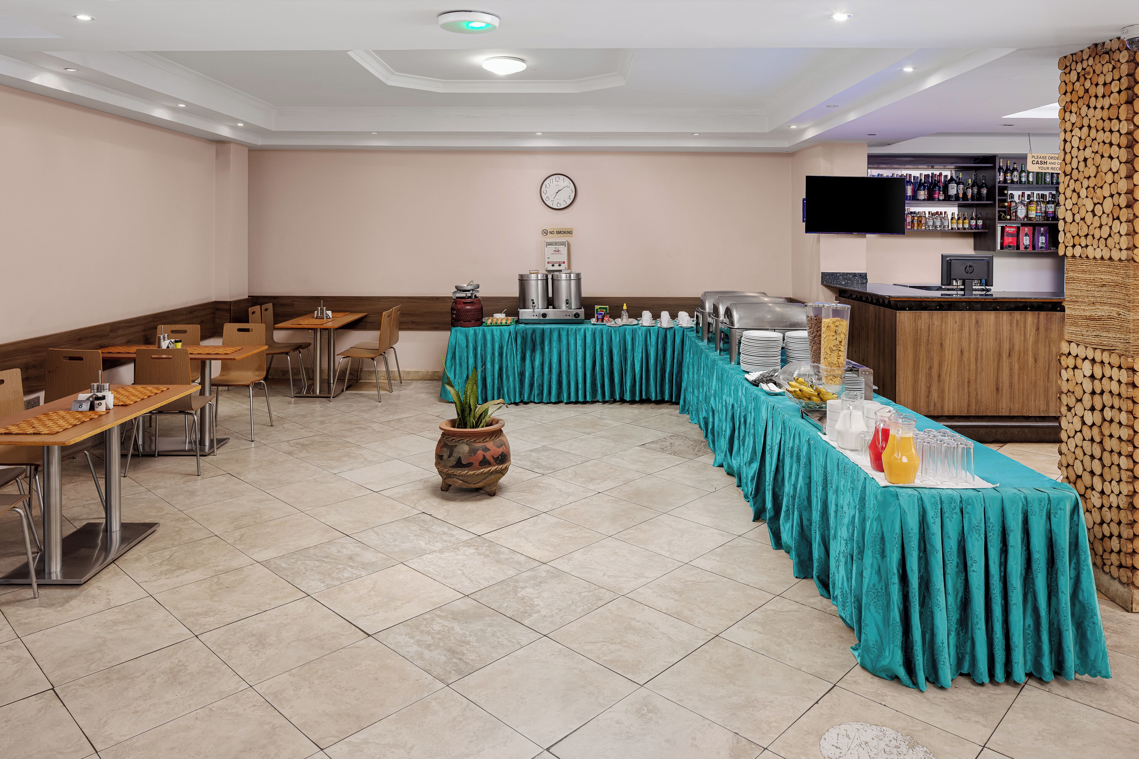 Zona pranzo di un hotel con un'ampia tavolo a buffet, posti a sedere e un orologio appeso al muro.