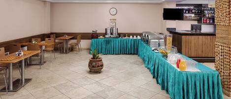 Zona pranzo di un hotel con un'ampia tavolo a buffet, posti a sedere e un orologio appeso al muro.