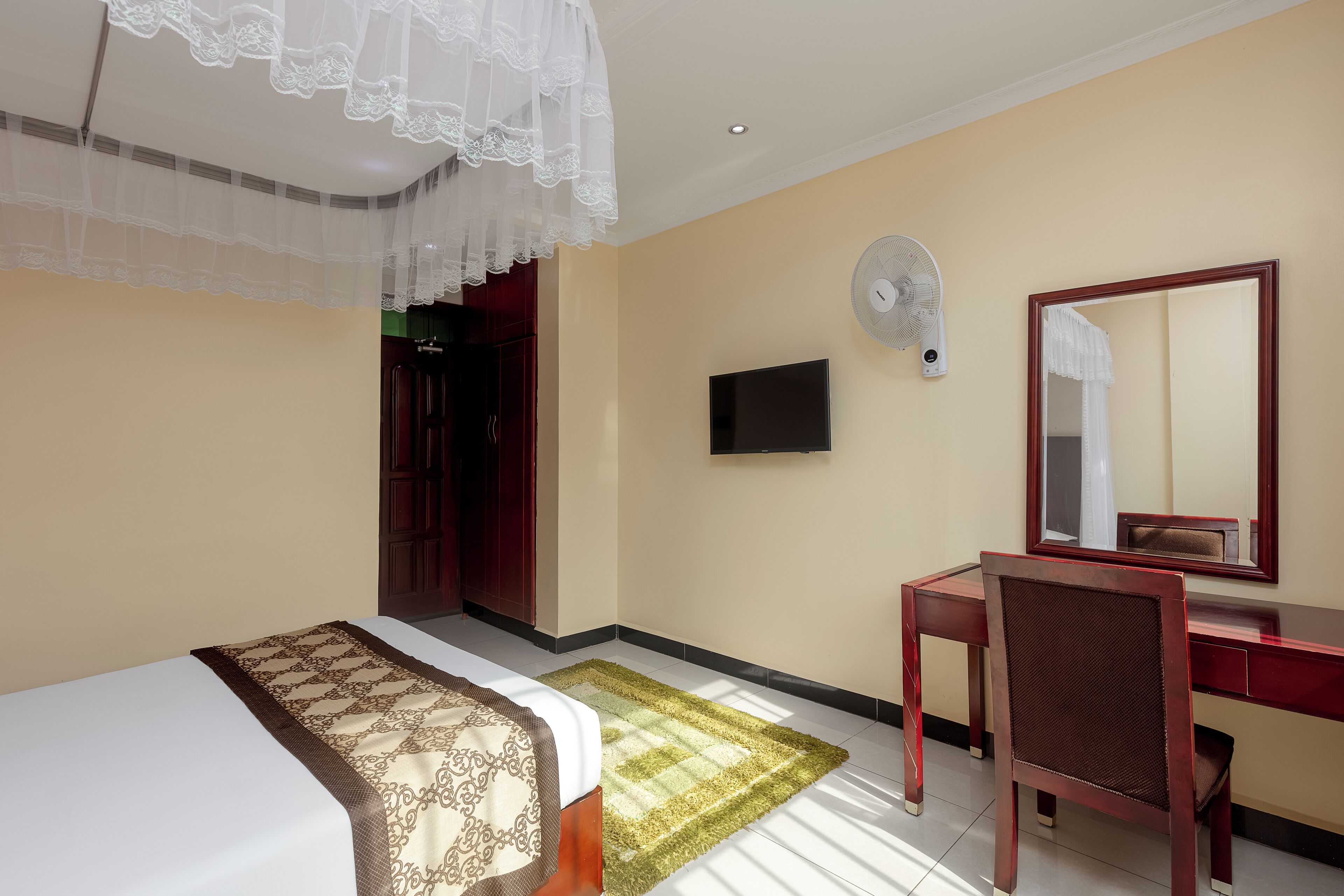 A hotel room with a bed, a desk, a chair, a television, and a mirror.
