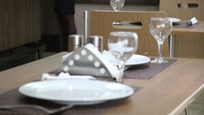 A dining table set with plates, cutlery, and glasses, with a wooden chair and a wine glass on the table. - Namayiba Park Hotel (Kampala)