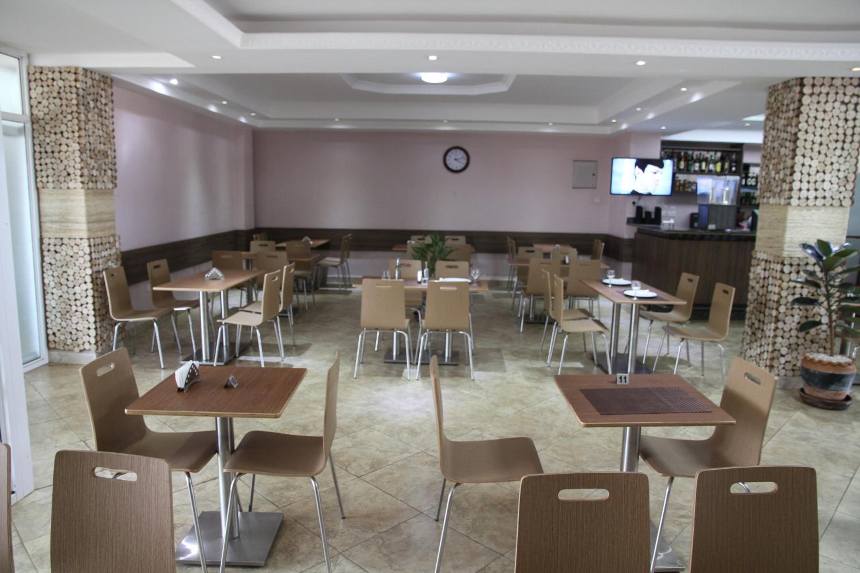 Un restaurante amplio con varias mesas y sillas, un reloj en la pared y una zona de bar al fondo.