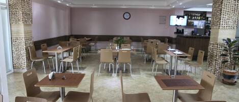 Un restaurante amplio con varias mesas y sillas, un reloj en la pared y una zona de bar al fondo.