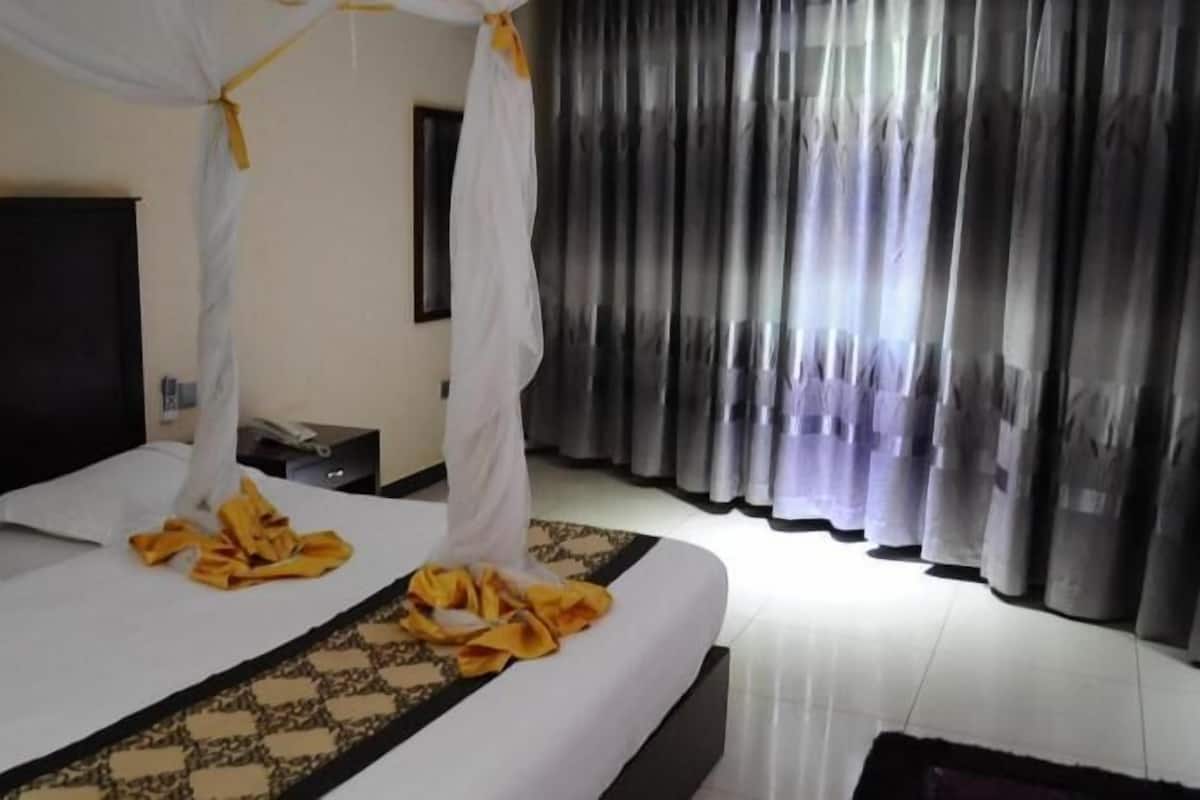 Una habitació d'hotel amb un llit, una taula de nit, una televisió i una cortina.