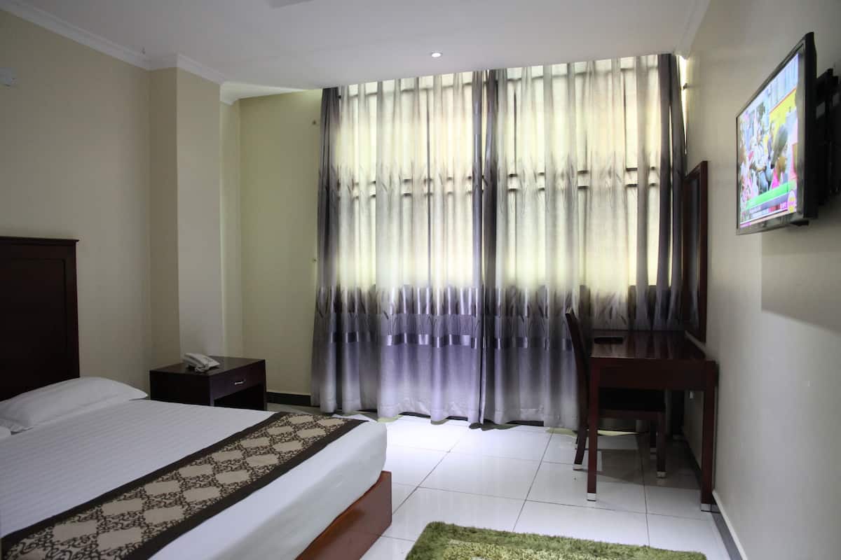 Habitació d'hotel amb llit, escriptori, cadira, televisió i finestra amb cortines.