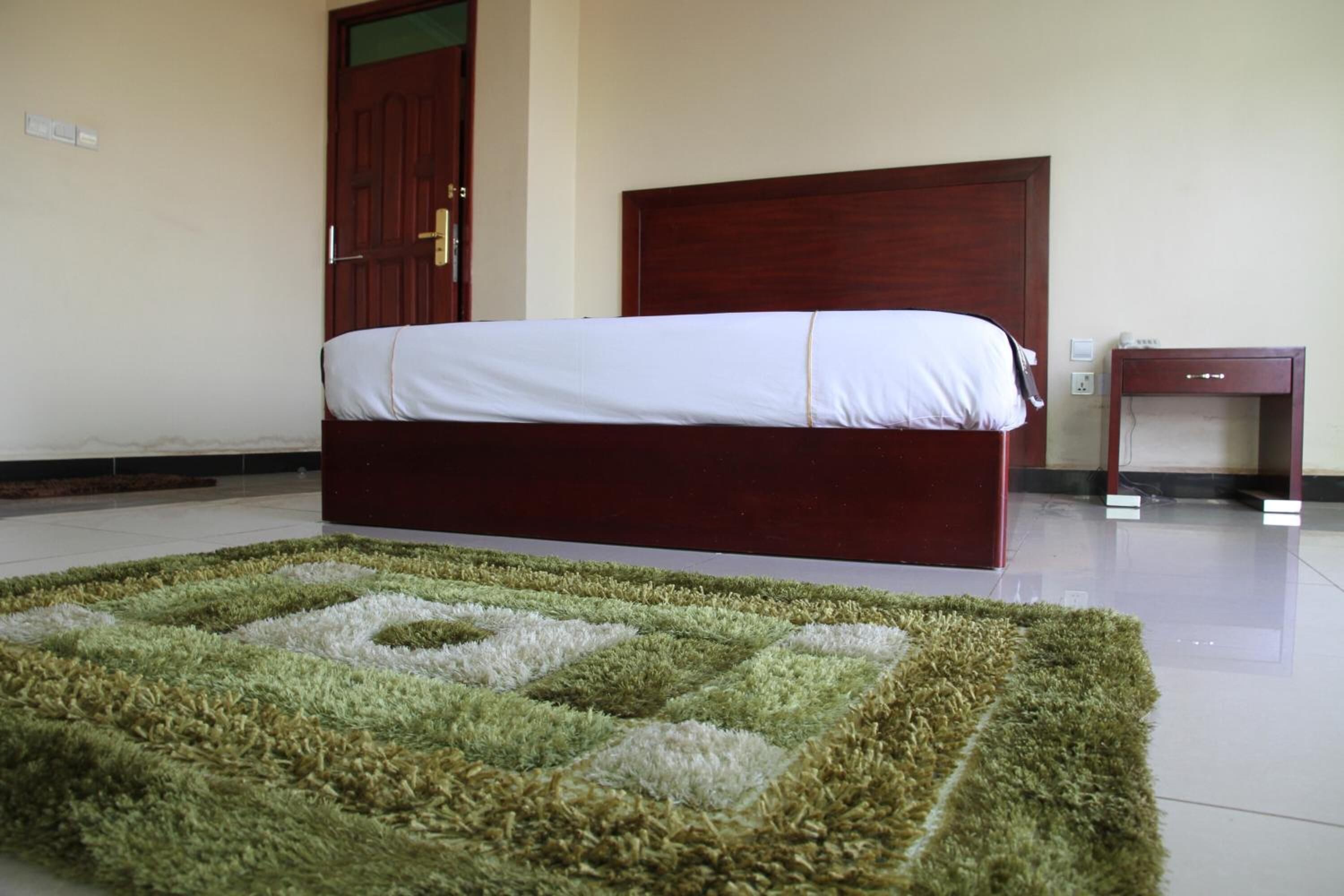 A bedroom with a bed, a wooden headboard, a small bedside table, and a patterned rug.