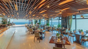 Un restaurant spacieux avec un plafond haut, un éclairage moderne et de grandes fenêtres offrant une vue sur la mer.