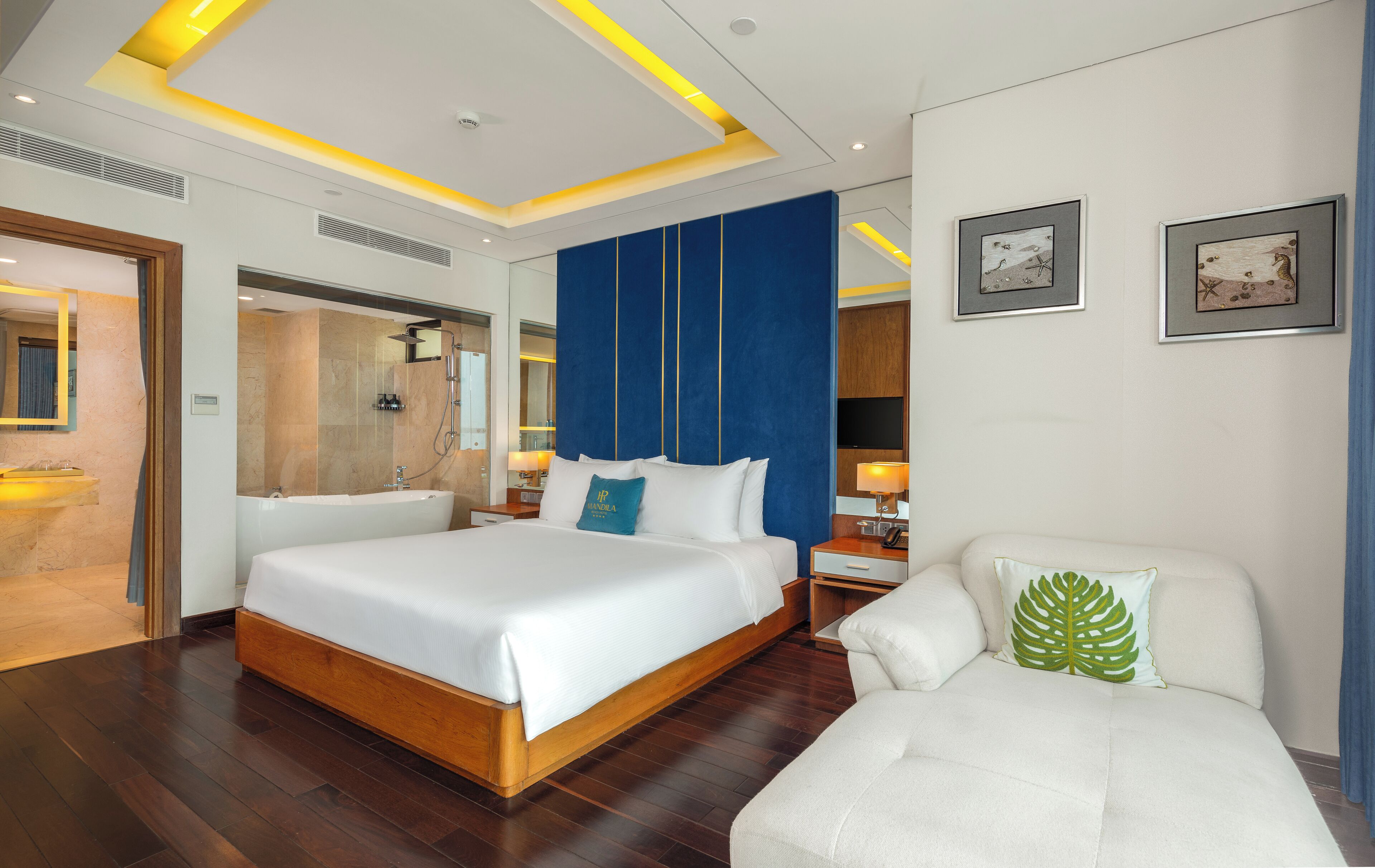 A hotel room with a large bed, a sitting area with a chair, a vanity with a mirror, and artwork on the walls.