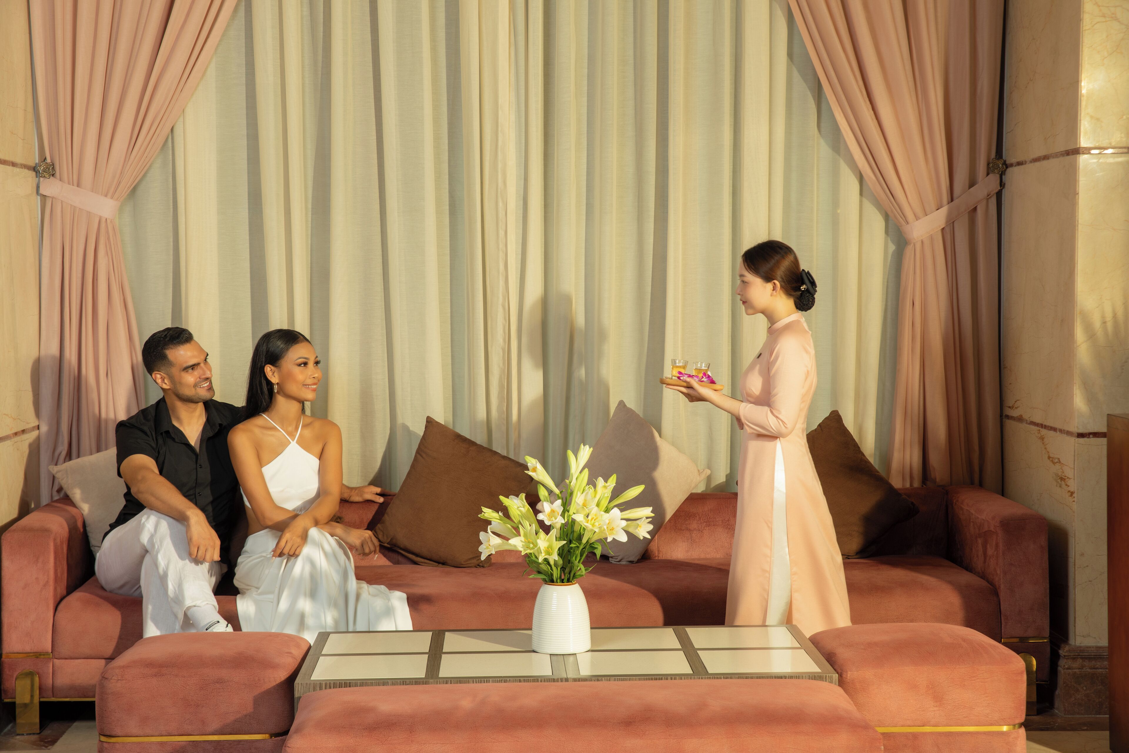 A room with a sofa, a coffee table, and a vase of flowers.
