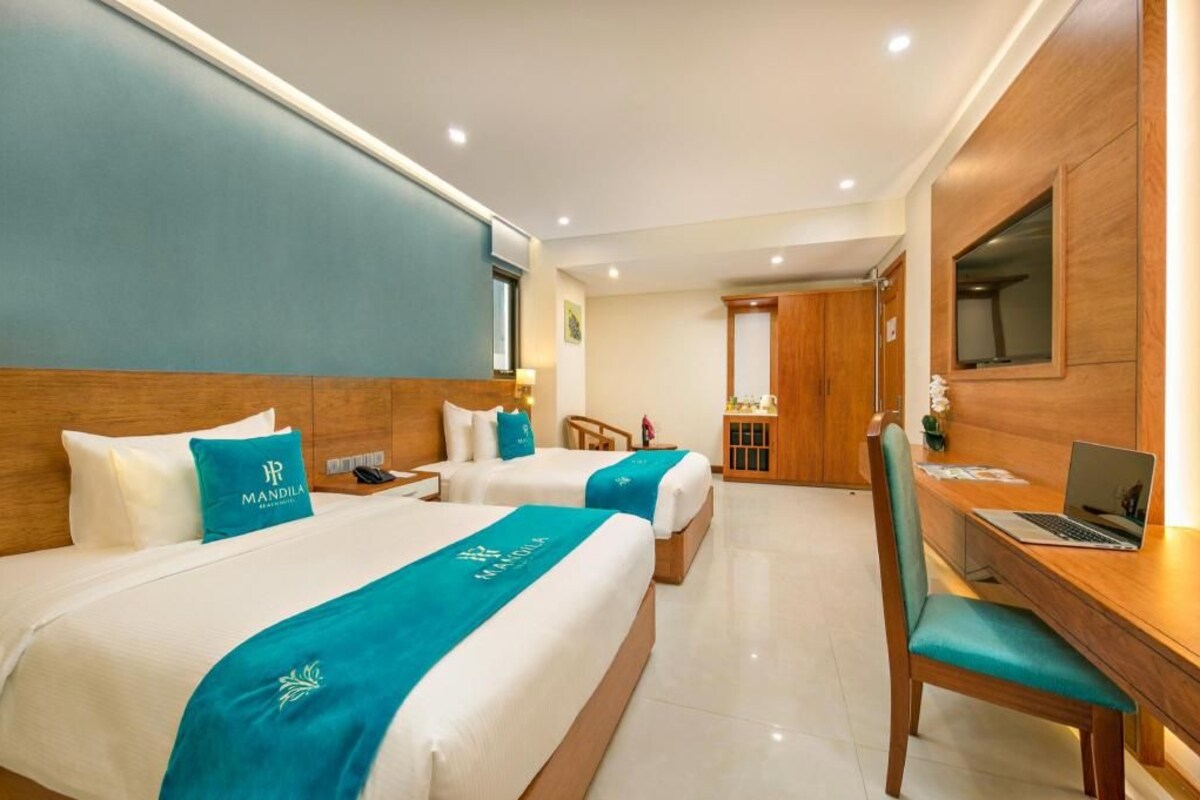 A hotel room with two beds, a desk with a laptop, and a mirror.