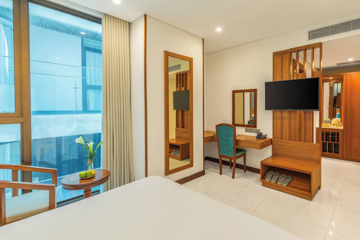 Een hotelkamer met een bed, een bureau, een stoel, een televisie en schoenenopslag.
