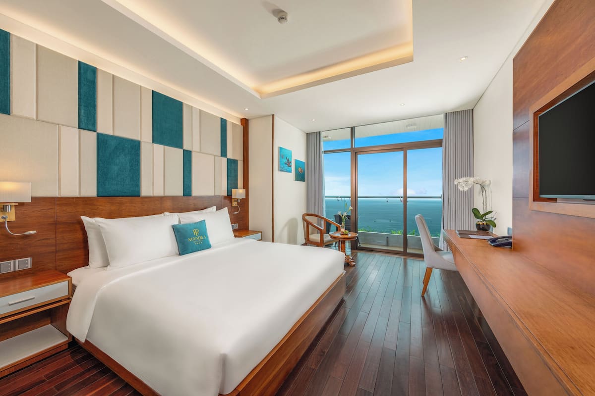 Een moderne hotelkamer met een groot bed, een bureau en uitzicht op zee.