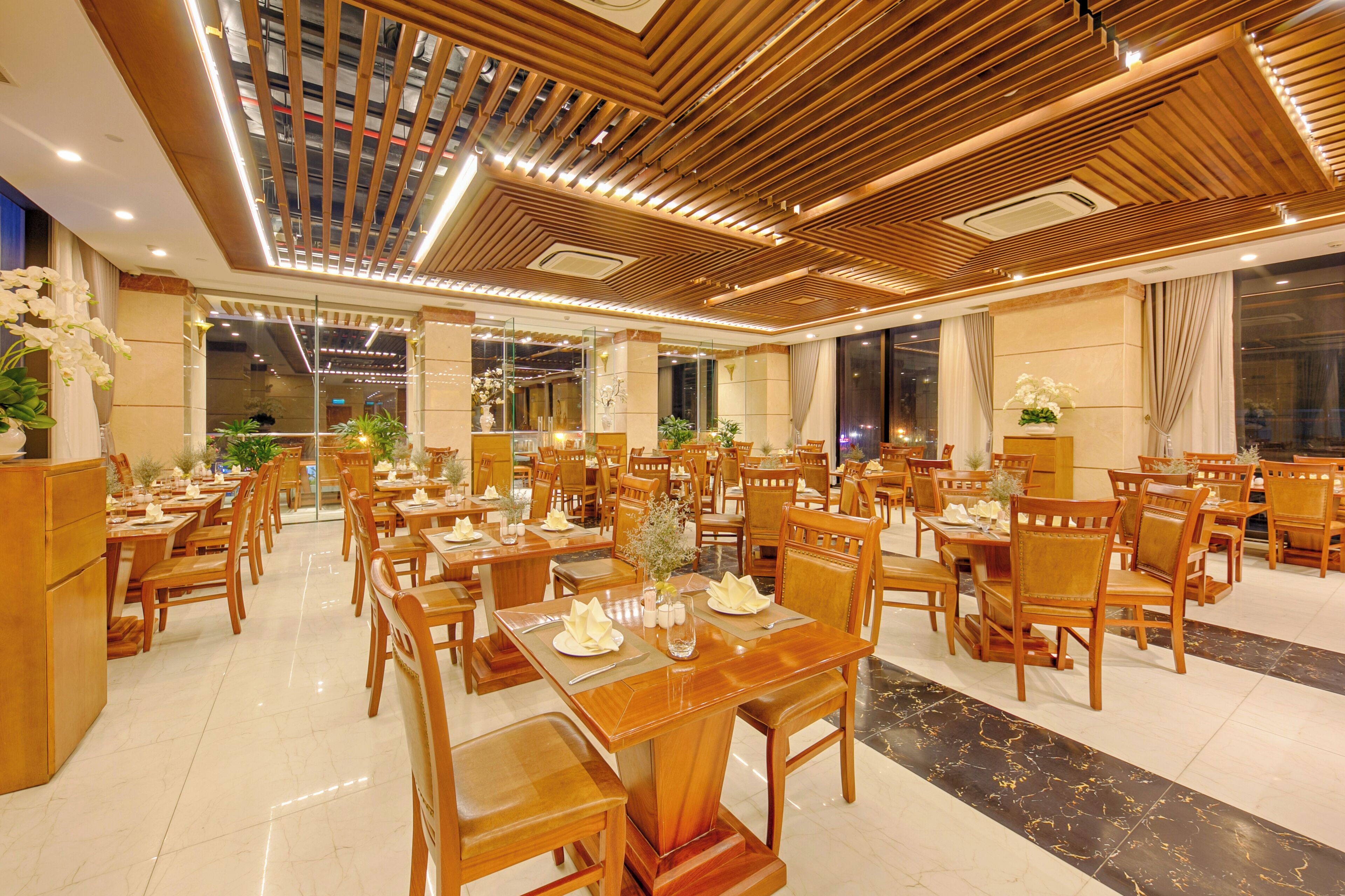 Un comedor amplio con mesas y sillas de madera, un diseño de techo moderno y ventanas grandes.
