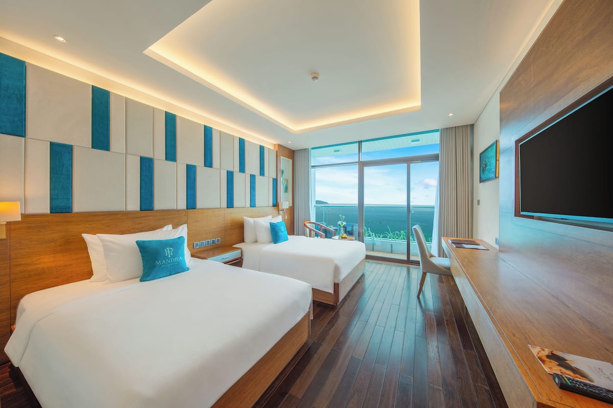 Een hotelkamer met twee bedden, een houten vloer, een grote televisie en een balkon met uitzicht.