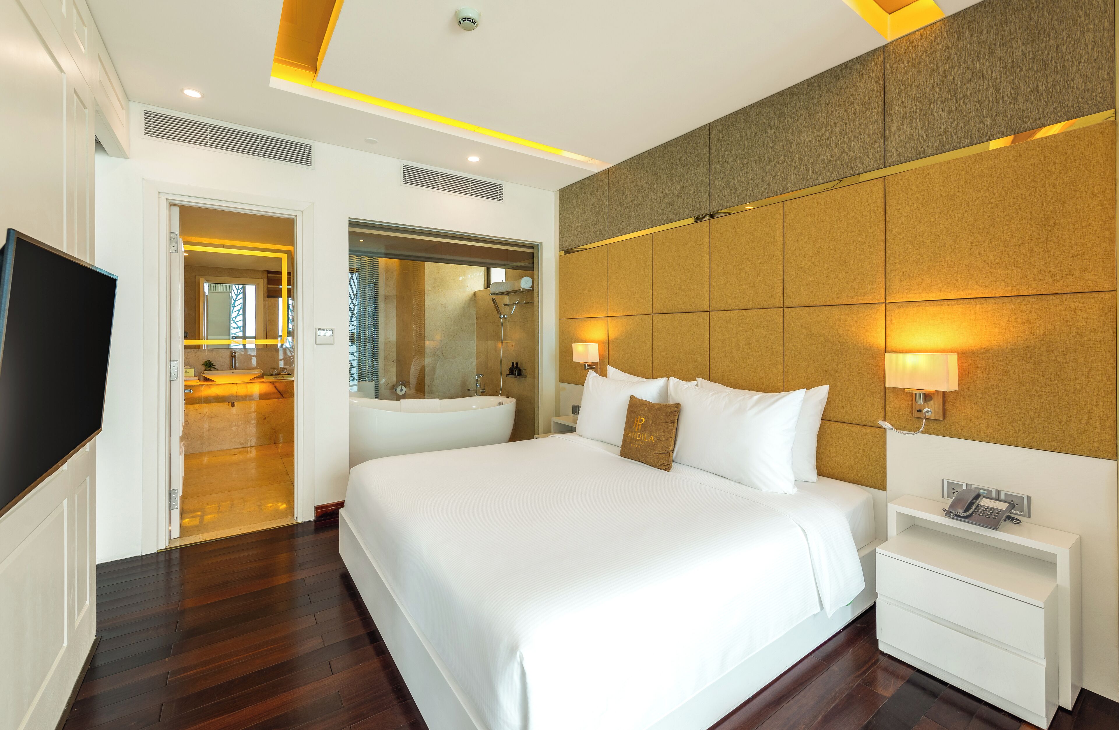 A hotel room with a large bed, bedside lamps, a TV, and a bathroom visible through an open door.