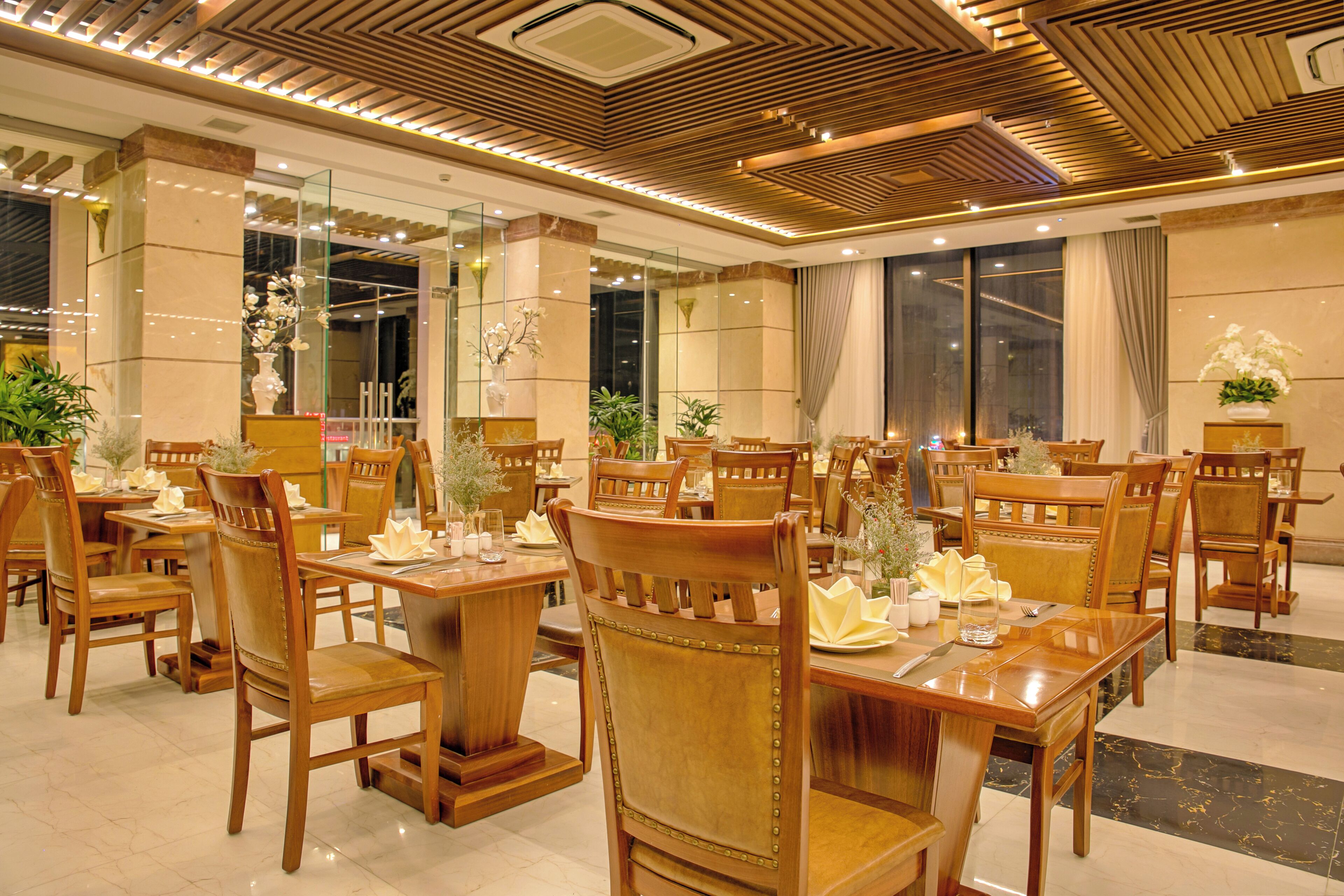 Un restaurant avec des tables et des chaises en bois, des cloisons en verre et des plantes décoratives.