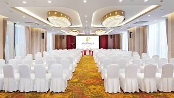 Un salón de conferencias con filas de sillas blancas, un escenario central con un banderín y candelabros.