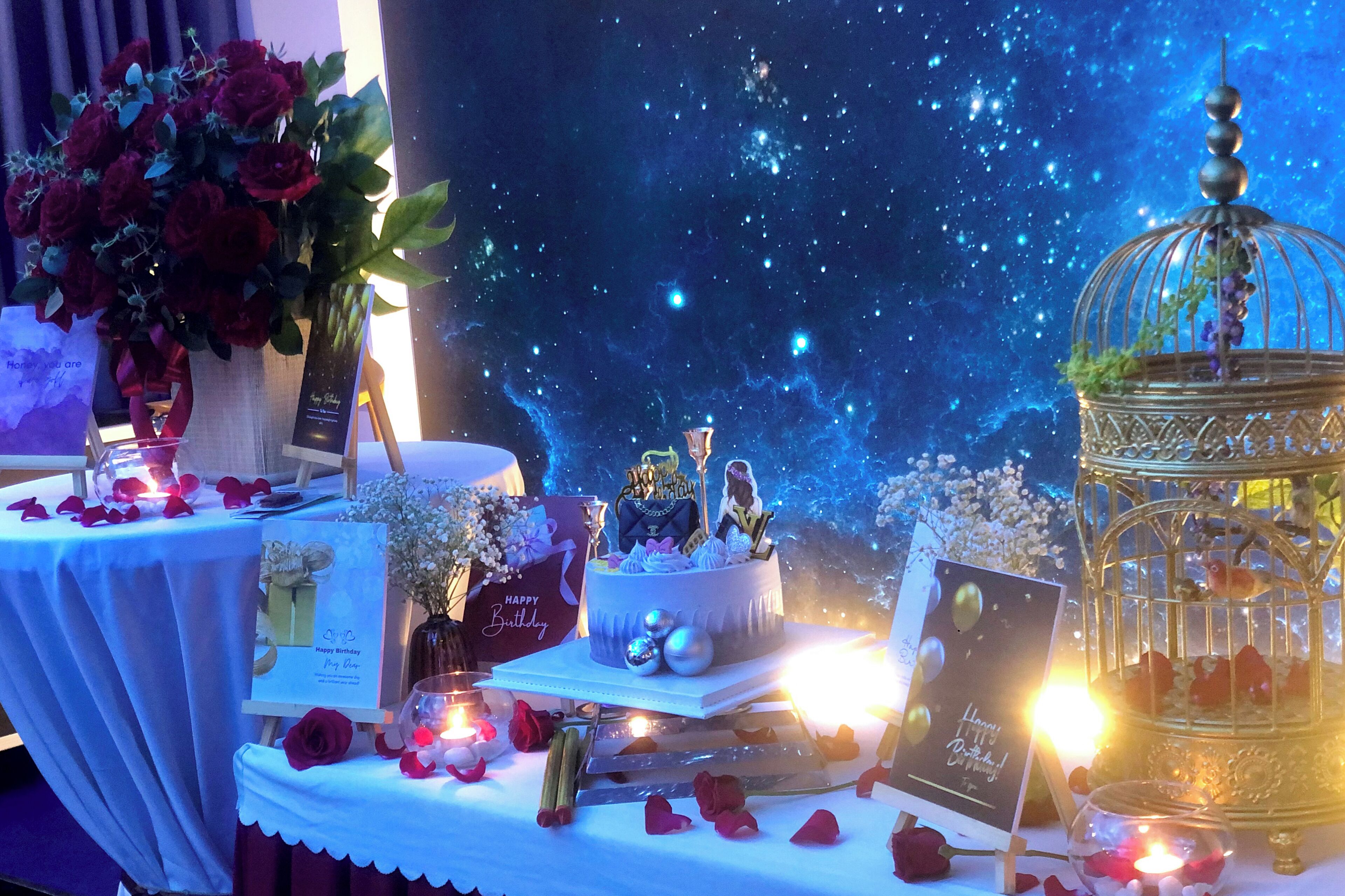 A table with a cake, a gift bag, a birdcage, and a bouquet of roses.