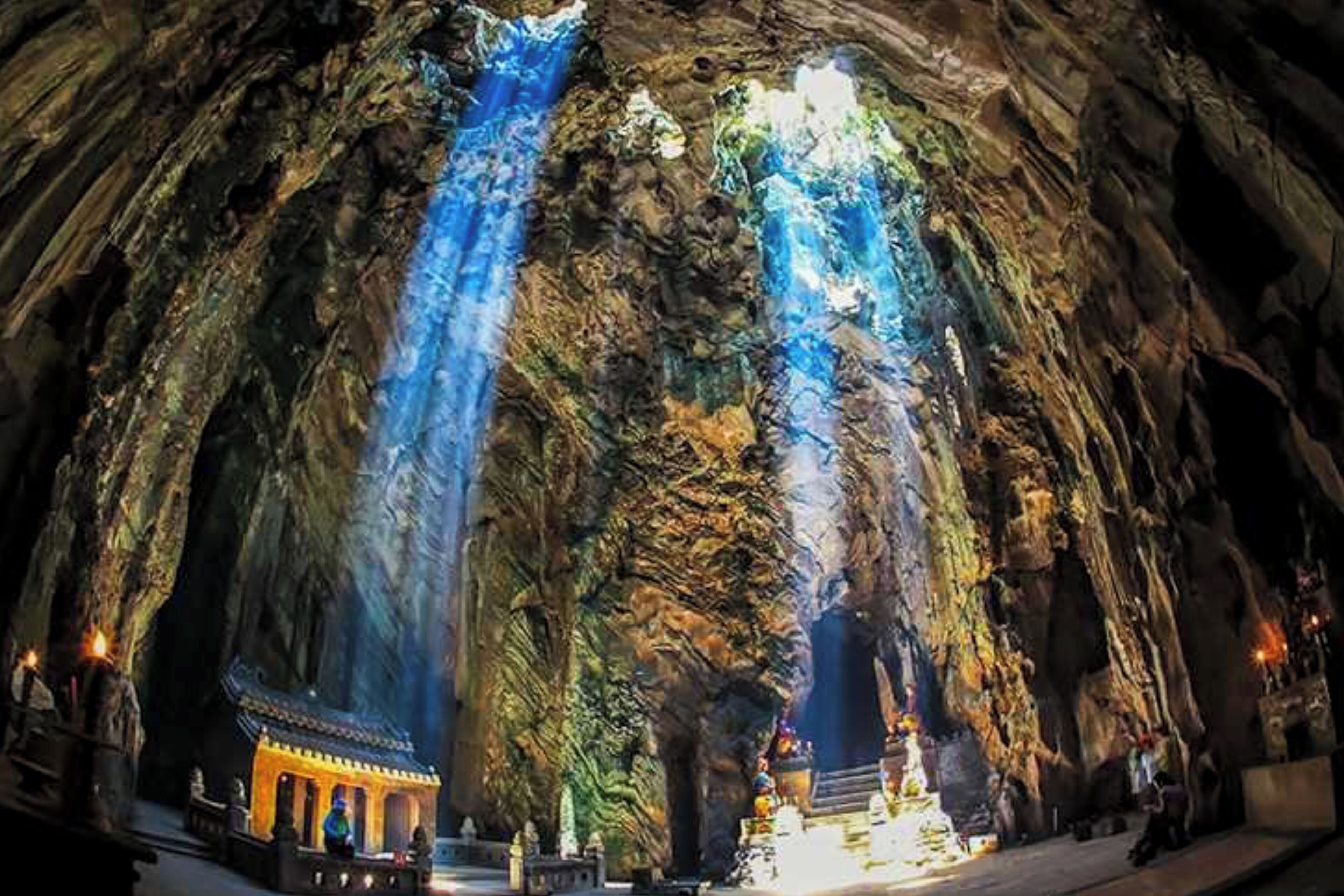 A cave with a waterfall and a small temple at the bottom.